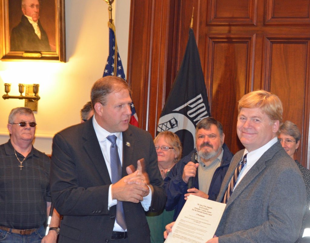 Governor Chris Sununu shaking the hand of David Morgan, President & CEO of future in Sight (formerly known as The New Hampshire Association for the Blind).  White cane and dog guide users are in the background.